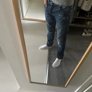 Dondup Jeans - Säljer ett par blå jeans från Dondup med snygga slitningar och patchade detaljer på knäna. Jeansen har klassisk femficksdesign, orange sömmar och en cool tvättad look. Passformen är rak och de har normal midja. Perfekta för en avslappnad streetstil.