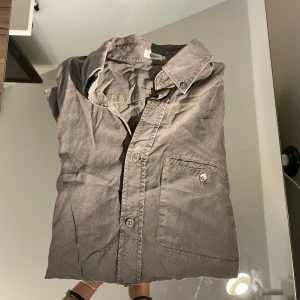 Grön skjorta från Filippa K i bomull - Stilren grå skjorta från Filippa K med klassisk krage och knappstängning framtill. Skjortan har en bröstficka med knapp och långa ärmar med manschett. Tillverkad i mjuk bomull som känns skön mot huden. Perfekt för en clean och avslappnad look.
