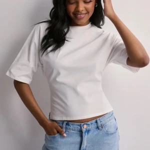 Vit croppad topp med knyt i ryggen - Säljer en vit croppad topp i bomull med korta ärmar och snygg knytning i ryggen. Toppen har öppen rygg och en clean, minimalistisk look som passar perfekt till jeans eller kjol. Enkel men ändå unik detalj med knytband bak. Köptes för 250kr!