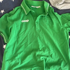 Grön pikétröja från Coop, storlek L - Säljer en grön pikétröja från Coop i storlek L. Den är sällsynt och används inte. Den är använd max 5 gånger. Nyskick
