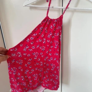 Rosa blommig linnetopp med smala band - Supersöt rosa linnetopp med små blommor i lila och vitt. Toppen har smala axelband och en luftig, flowy passform som är perfekt för varma dagar. Materialet känns lätt och skönt mot huden. Perfekt för dig som gillar färg och mönster!