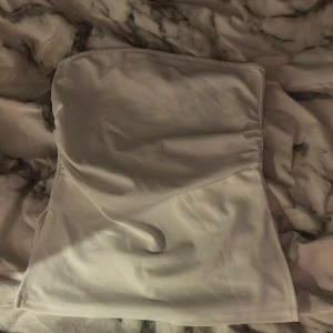 Vit tubtopp från 157 - Säljer en stilren vit tubtopp från 157. Toppen är axelbandslös och har en enkel, slät design i mjukt tyg. sitter bra mot kroppen men jag använder den aldrig längre och är använd cirka 2 gånger❣️ jättefin nu inför sommaren!! köpte den även för 150kr så därför ja säljer för 50kr.