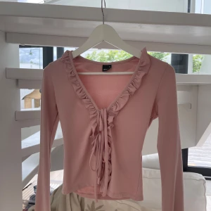 Rosa omlottopp med volang och knyt - Supersöt ljusrosa topp från Gina Tricot med volangkant längs v-ringningen och knyt framtill. Långärmad och i mjukt bomullsmaterial. Perfekt för dig som gillar romantiska detaljer och en feminin look. Säljer på grund av att jag inte har användning till tröjan! 💗