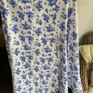 Vit långklänning med blåa blommor - Superfin långkjoli vitt med blåa blommor över hela tyget. Perfekt för sommarens alla tillfällen! Materialet känns mjukt och svalt mot huden.