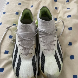 Adidas Crazyfast elite vita fotbollsskor - Snabba Adidas Crazyfast elite fotbollsskor i vitt med svarta detaljer och neongul sula. Skorna har låg profil, snörning och ovandel i syntetmaterial. Perfekta för dig som vill sticka ut på planen med stil och fart. Pris ej hugget i sten.