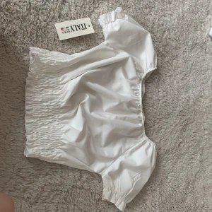 Vit offshoulder topp från ITALY MODA - Supersöt vit offshoulder topp från ITALY MODA med smockad midja och kort puffärm. Perfekt för dig som gillar romantisk och trendig stil. Tunn och luftig bomull som känns fräsch och somrig. Säljes med tag kvar!