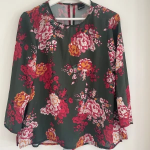 Blommig blus från Gina Tricot - Supersnygg blommig blus från Gina Tricot i grönt med stora röda, rosa och gula blommor. Blusen har rund halsringning, långa ärmar och är tillverkad i ett lätt tyg. Perfekt för dig som vill sticka ut med färg och mönster! Har lite vita streck efter slitage men syns knappt.