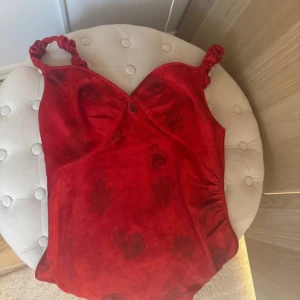 Röd blommig kortklänning från Adoore - Supersöt röd kortklänning från Adoore med blommigt mönster och twistade axelband. Klänningen har en lätt v-ringning och figurnära passform, perfekt för dig som vill sticka ut. Materialet känns mjukt och följsamt mot huden. Så fin! Insydd så sitter så fint mer likt 36 än 40🦩👙🍸🌴🧁🫶🏼
