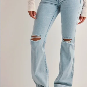 Ljusblå bootcut jeans med hål - Säljer ett par ljusblå bootcut jeans med slitna hål över knäna och broderade detaljer på bakfickorna från Nelly köpte för 700 kr💓Jeansen har normal passform och är tillverkade i klassisk denim. De är en aning slitna nere vid byxkanterna men inget man tänker på mycket, storlek 34💐