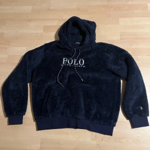 Mörkblå fleece hoodie Polo Ralph Lauren - Mysig mörkblå hoodie från Polo Ralph Lauren i fluffig fleece med broderad logga på bröstet och ärmen. Tröjan har huva med snörning, känguruficka och ribbade muddar. Perfekt för kalla dagar när du vill vara både chill och snygg. Oanvänd, pris kan diskuteras