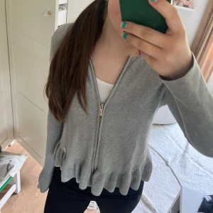 Grå kofta med volangkant från Massimo Dutti - Säljer en ljusgrå kofta från Massimo Dutti med dragkedja framtill och volangkant nedtill. Den är i storlek 146 men är själv 158 och den passar. Skulle kanske säga XXS eller en 158/164💘