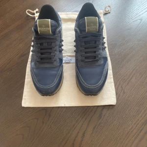 Valentino Rockrunner sneakers i marinblått skinn - Säljer ett par Valentino Rockrunner sneakers i marinblått skinn med svarta detaljer och ikoniska nitar på sidorna. Skorna har snörning, rund tå och platt sula. Kommer med original dustbag. Pris är inte hugget i sten och kom dm om du har några frågor 