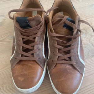 Bruna sneakers från Björn Borg - Säljer ett par bruna skinnsneakers från Björn Borg med vita detaljer och svart häl. Skorna har snörning, rund tå och platt sula. Perfekta för en avslappnad stil och funkar till det mesta🤗
