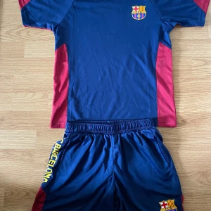 FC Barcelona fotbollströja och shorts - Säljer en blå och röd FC Barcelona fotbollströja med klubbmärke på bröstet och texten 'BARÇA' på ryggen. Matchande shorts med klubbmärke och texten 'FC BARCELONA' på sidan. Tillverkad i 100% polyester. I storlek M (passar för 11-13 åringar), för ENDAST 175 för både shorts och T-shirt. Pris kan diskuteras. Inga defekter! 