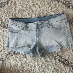 Ljusblå jeansshorts med fransar - Säljer ett par ljusblå jeansshorts med slitna detaljer, perfekta för sommaren. Klassisk knapp- och dragkedjestängning framtill. Dom är lågmidjade och skitsnygga! Midjemått rakt över: 38cm💞💞