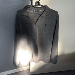 Grå tröja med dragkedja från Polo Ralph Lauren - Säljer en stilren grå långärmad tröja från Polo Ralph Lauren med halv dragkedja och liten broderad logga på bröstet. Perfekt för en avslappnad men snygg look. Klassisk passform och mjukt material. Pris kan diskuteras.