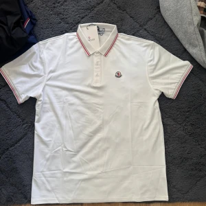 Vit piké t-shirt från Moncler - Säljer en klassisk vit piké t-shirt från Moncler med röd och blå rand på krage, helt ny, 999kr