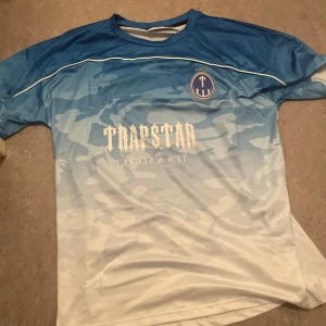  Trapstar t shirt  - Säljer en snygg kortärmad fotbollströja från Trapstar i blått och vitt med kamouflagemönster. Tryck med Trapstar-logga och siffran 23 på ryggen. Perfekt för dig som gillar streetwear och sportig stil.