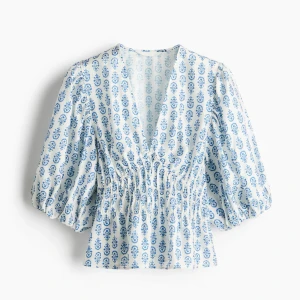 Populär Vit och blå blus från h&m med puffärm och smock - Säljer en vit blus med blått mönster och v-ringning. Blusen har trekvarts puffärmar och smockad midja som ger en snygg siluett. Perfekt för dig som gillar en luftig och trendig stil. Helt ny med prislapp kvar! Den är super populär därav priset. Priset går att diskuteras❣️