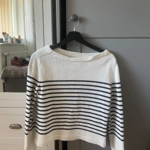 Vit och marinblå randig stickad tröja - Säljer en vit stickad tröja med marinblå horisontella ränder. Tröjan har lång ärm och en något croppad passform. Perfekt för en avslappnad och stilren look.