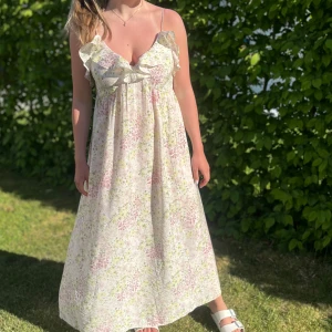 Blommig långklänning med volang - Söt långklänning med blommigt mönster i ljusa toner. Klänningen har smala axelband, volangdetaljer vid bysten. Den är i storlek L men passar mig som vanligtvis har S 