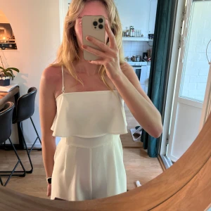 Vit byxdress med volang från Gina Tricot - Säljer en söt vit byxdress från Gina Tricot med smala axelband (avtagbara) och volangdetalj över bysten. Dragkedja i ryggen och fickor i fram. Aldrig använd så jättefint skick! Den är i storlek 36, men för kort på mig som är 178 därav säljer jag den. 