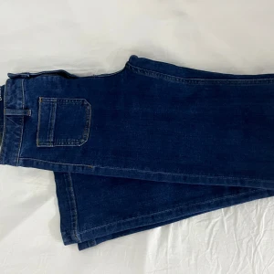 Mörkblå bootcut jeans Camille W27 L32 - Snygga mörkblå jeans i modellen bootcut från Camille. Jeansen har klassisk femficksdesign, normal passform och stängs med dragkedja och knapp. Perfekta för dig som gillar en tidlös look med lite utsvängda ben. 