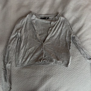 Grå croppad kofta från 157 - Grå tunn och croppad kofta från 157 med långa ärmar och knappar framtill. Perfekt att ha över ett linne eller t-shirt. Enkel och stilren design som passar till mycket.