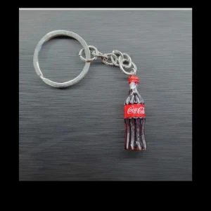 Nyckelring med Coca-Cola flaska - Säljer en cool nyckelring med en miniatyr av en klassisk Coca-Cola flaska. Flaskan är detaljerad med röd etikett och silverfärgad ring. Perfekt accessoar för dig som gillar unika detaljer.