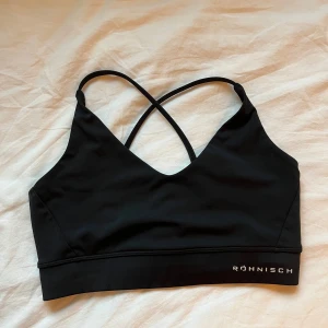 Svart sport-bh från Röhnisch - Svart sport-bh från Röhnisch med smala korsade axelband i ryggen, inte justerbara band. Röhnisch märket har lite slitage annars i bra skick!☺️Passar XS/S.