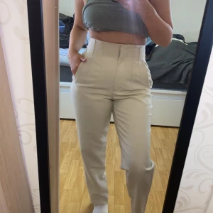 Beiga kostymbyxor med hög midja - ZARA Säljer ett par stilrena beiga kostymbyxor med hög midja och raka ben. Byxorna har diskreta sömmar framtill och stängs med dragkedja och hyska. Perfekta för en clean och snygg look.