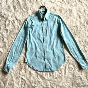Ljusblå skjorta från Ralph Lauren - Säljer en ljusblå skjorta från Ralph Lauren med klassisk krage och broderad logga på bröstet. Skjortan har lång ärm, knappar framtill och är i super slim fit-modell. I bra skick