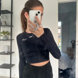 Svart croppad långärmad träningstopp - Säljer en assnygg svart, croppad långärmad träningstopp med ribbad struktur. Tröjan har en tight passform och en liten vit NA-logga på bröstet. Perfekt till typ gymmet eller idrotten. Hittar inte storleken men skulle tro xxs/xs