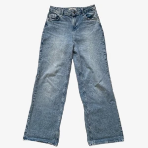 Blå wide leg jeans från Stradivarius - Säljer ett par ljusblå jeans från Stradivarius med hög midja och raka, vida ben. Klassisk femficksmodell med knapp och dragkedja framtill. Perfekta för en avslappnad och trendig look.
