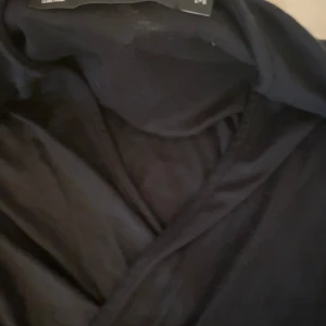 Svart omlottopp med lång ärm - Säljer en svart omlottopp med långa ärmar. Toppen har en knytning i midjan och är tillverkad i ett mjukt, stretchigt material. Perfekt för en stilren och enkel look.