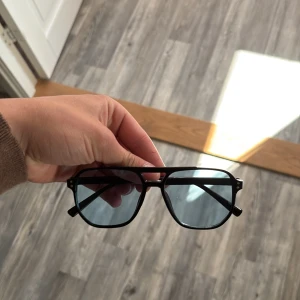 Svarta bågar med blåa glas lika tom ford - Stilrena svarta solglasögon med pilotformade bågar och mörka glas. Klassisk design som passar till många olika outfits. Bågarna är i plast och har en modern känsla.