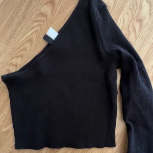 Svart oneshoulder topp - Säljer en svart ribbad oneshoulder topp med lång ärm. Toppen är croppad och har en tight passform.
