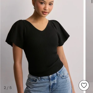 Svart ribbad topp med puffärmar och knyt i ryggen - Säljer en svart ribbad topp med v-ringning och korta puffärmar från only. Toppen har en snygg detalj med rosett i ryggen. Använd fåtal gånger, känns som ny utan några defekter. Skriv för fler frågor🩷