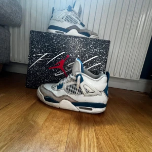 Nike Air Jordan 4 Retro 'Military Blue' - Säljer ett par Nike Air Jordan 4 Retro 'Military Blue' med vit ovandel, blå och grå detaljer samt meshpaneler. Skorna har snörning, rund tå och platt sula. Klassisk Jordan-logga på hälen och originalkartong medföljer.