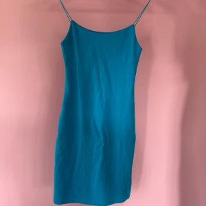 Blå klänning med smala axelband från Zara - Säljer en enkel och stilren blå klänning från Zara med smala axelband och rak passform. Perfekt för varma dagar eller att styla med en jacka. Klänningen är knälång och har en minimalistisk look. Oanvänd men utan lapp!