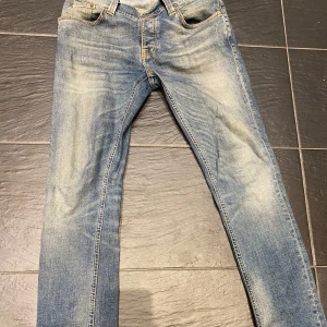 Nudie jeans - Säljer ett par klassiska blå jeansbyxor med snygga slitningar och ljusare partier framtill och baktill. Byxorna har fem fickor, dragkedja och knapp i midjan samt raka ben. Perfekta för en avslappnad stil.