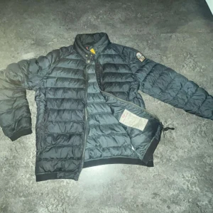 Svart pufferjacka från Parajumpers - Säljer en svart pufferjacka från Parajumpers med hög krage och dragkedja. Jackan har ett emblem på ärmen och en bröstficka med dragkedja. Perfekt för kyliga dagar.