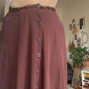 Brun kjol med knappar - Säljer en brun kjol med knappar framtill och hög midja. Kjolen har en lätt A-linjeform och är tillverkad i ett mjukt tyg som känns bekvämt. Perfekt att styla med en enkel topp eller stickad tröja. . 💌 Skick: Bra begagnat skick – allt i fint skick förutom en saknad knapp. 🌿 Rök- och djurfritt hem  📍 Upphämtning i Malmö eller skickas! 