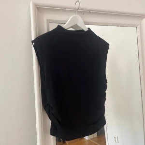 Svart ärmlös topp - Säljer en svart ärmlös topp med rund hög halsringning. Enkel och stilren design som passar till många olika outfits. Perfekt för varmare dagar eller som lager under en kavaj.