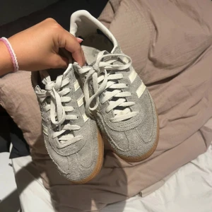 Grå Adidas Spezial sneakers - Säljer ett par grå Adidas Spezial sneakers med vita ränder och snörning. Skorna har en klassisk design med mockaöverdel och gummisula i brunt. Perfekta för dig som gillar retrostil och vill ha något bekvämt till vardags.
