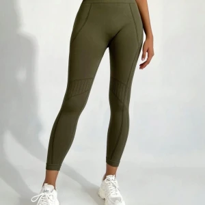 Leggings - Snygga olivgröna leggings med hög midja och ribbade detaljer längs benen. De har en tight passform och är perfekta för träning eller en sportig vardagslook. Tillverkade i ett stretchigt syntetmaterial som ger bra rörelsefrihet.