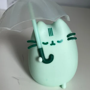 Pusheen regn figurine - Pusheen-figur i mintgrönt med ett genomskinligt paraply. Figuren är ca 9 cm
