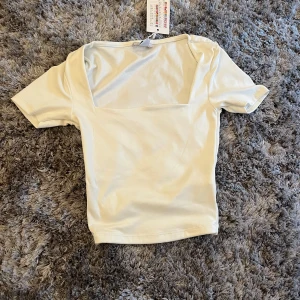 Vit topp med fyrkantig ringning - Vit topp som är lite kortare och är i ett lite glansigt snyggt tyg! Helt ny aldrig använd 