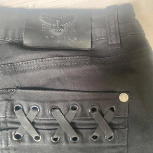 Svarta bootcut-byxor med snörningsdetalj från D.N.A Premium - Säljer ett par svarta bootcut-byxor från D.N.A Premium med snygg snörningsdetalj på bakfickan. Byxorna har låg midja och klassisk femficksdesign. 