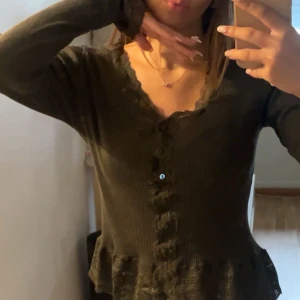 Mörkgrön kofta med volangkant - Säljer en mörkgrön ribbad kofta med v-ringning och knappar framtill från rosemunie i storlek xs. Tröjan har långa ärmar och en söt volangkant nedtill.